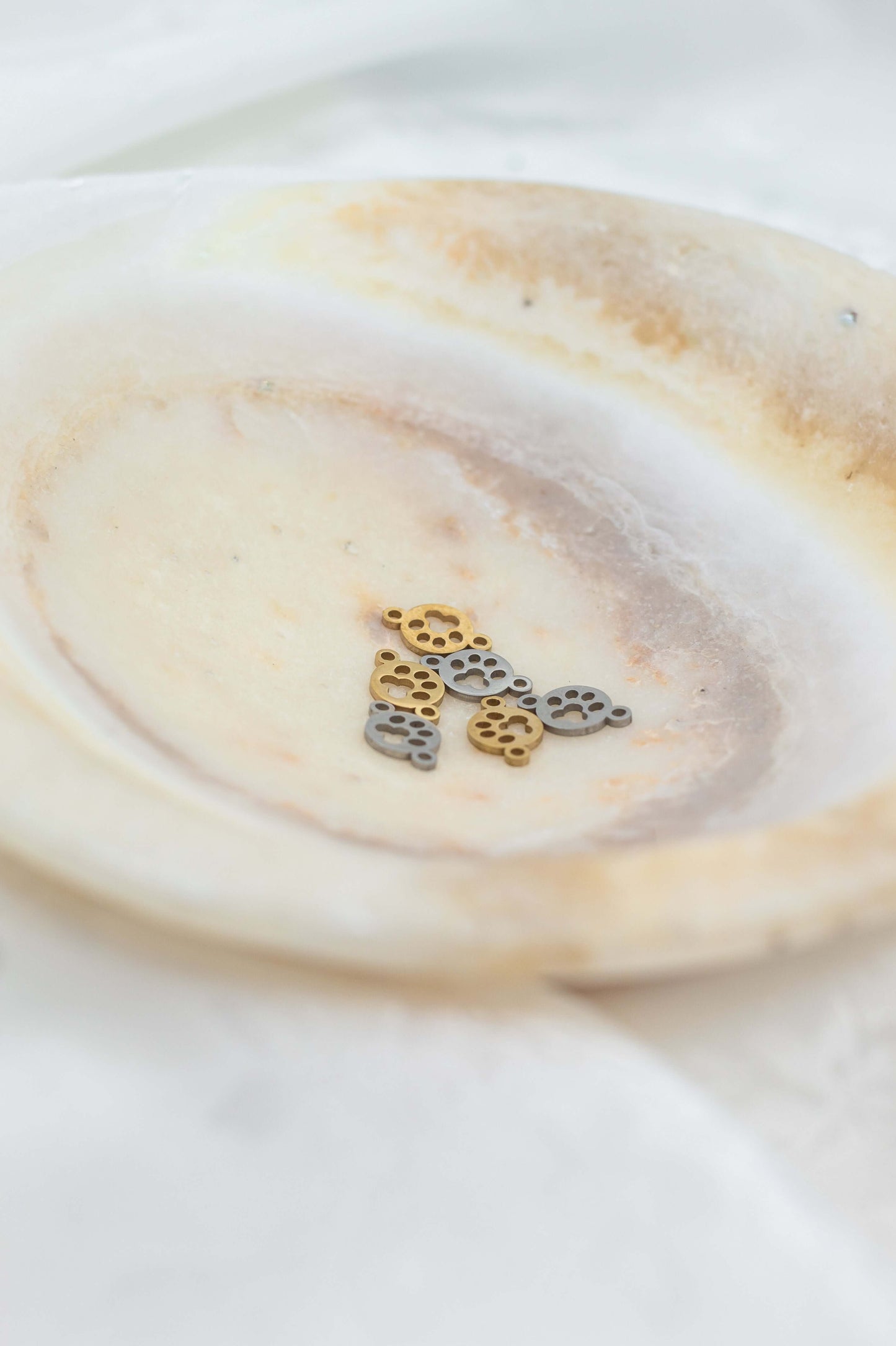 Paw Print Connector Charm in gold and silver on a decorative plate, perfect for pet lovers' jewelry.