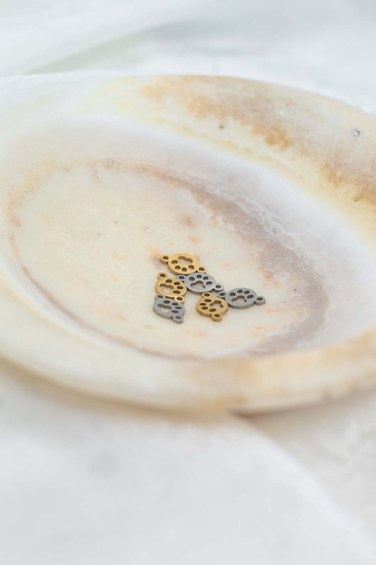 Paw Print Connector Charm in gold and silver on a decorative plate, perfect for pet lovers' jewelry.